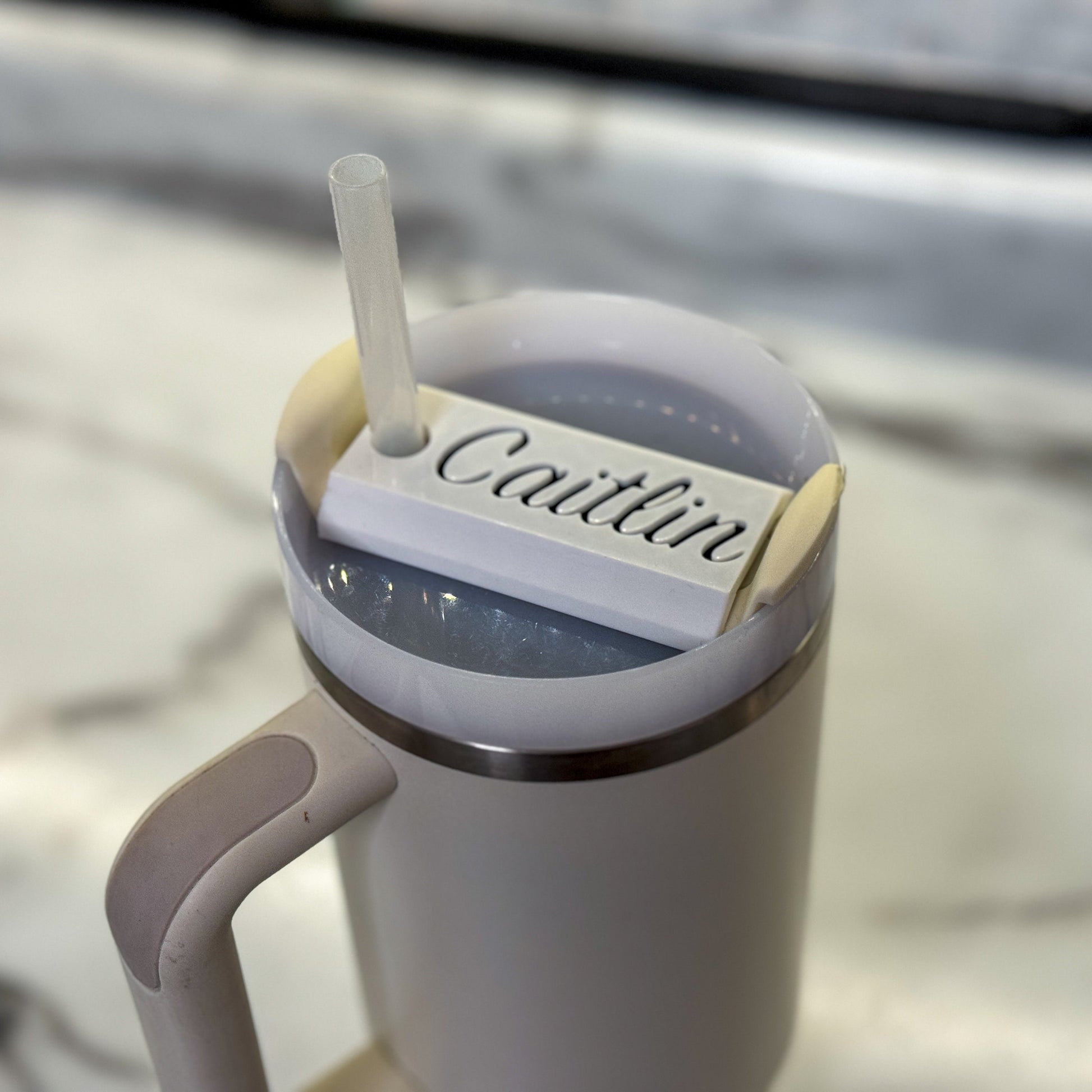 A white name plate with black lettering that says caitlin on top of a 64oz stanley tumbler