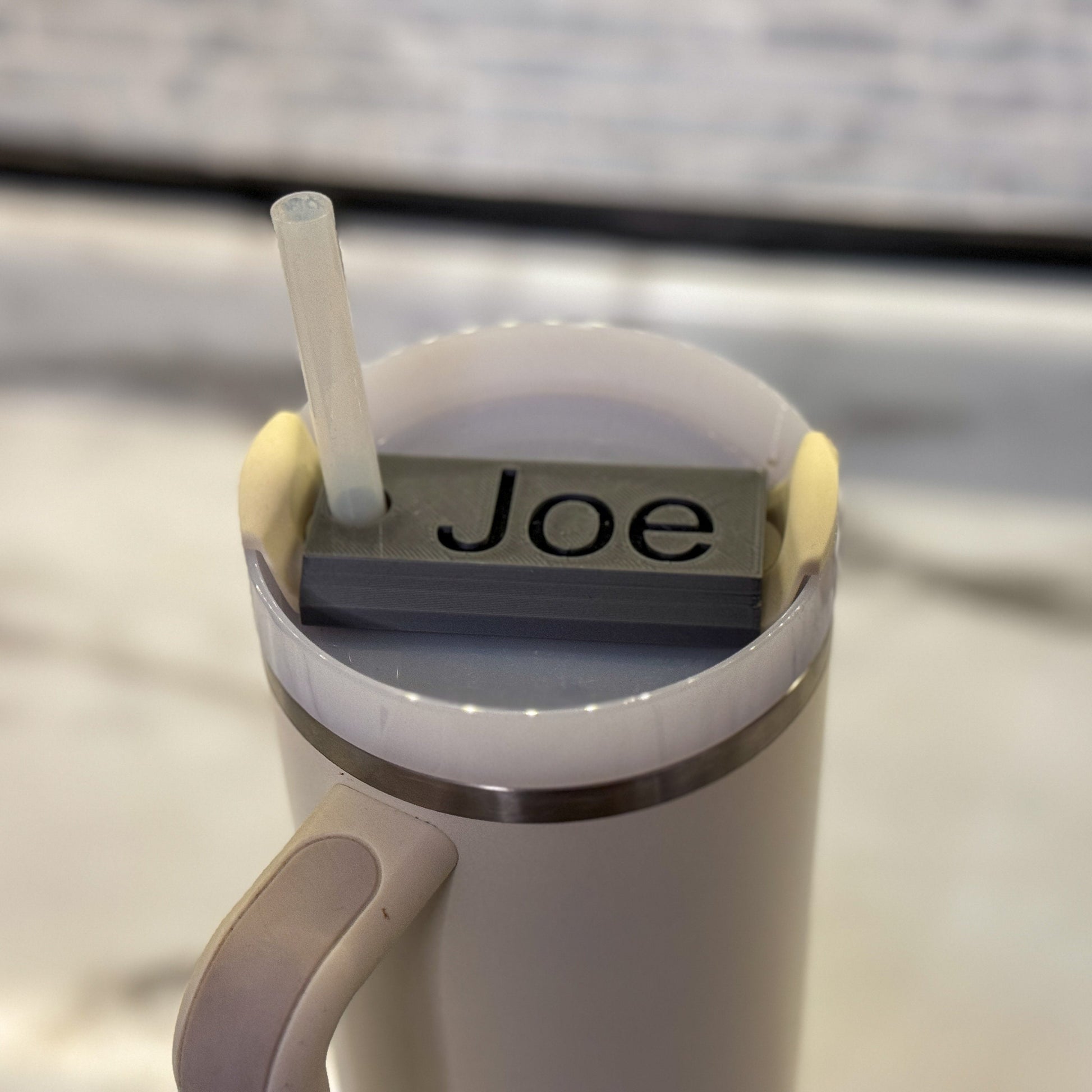 A grey name plate with black lettering that says Joe on top of a 40oz stanley tumbler