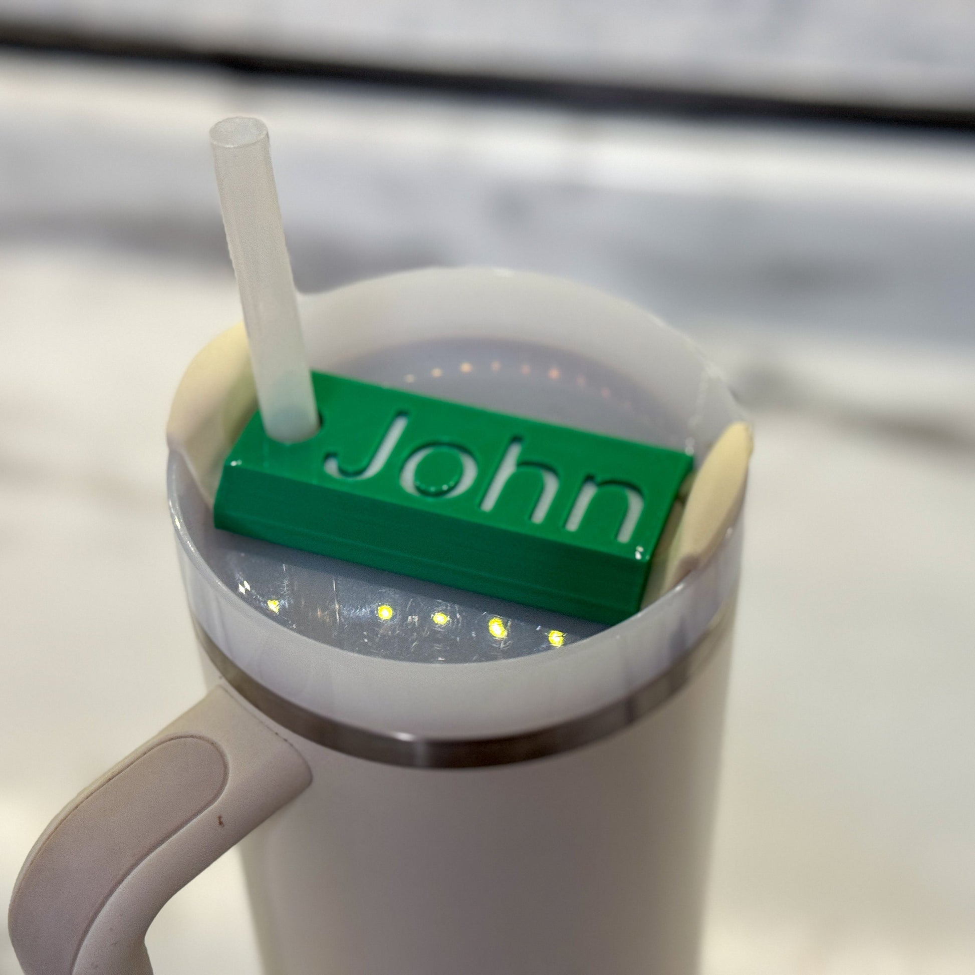 A green name plate with white lettering that says John on top of a 64oz stanley tumbler