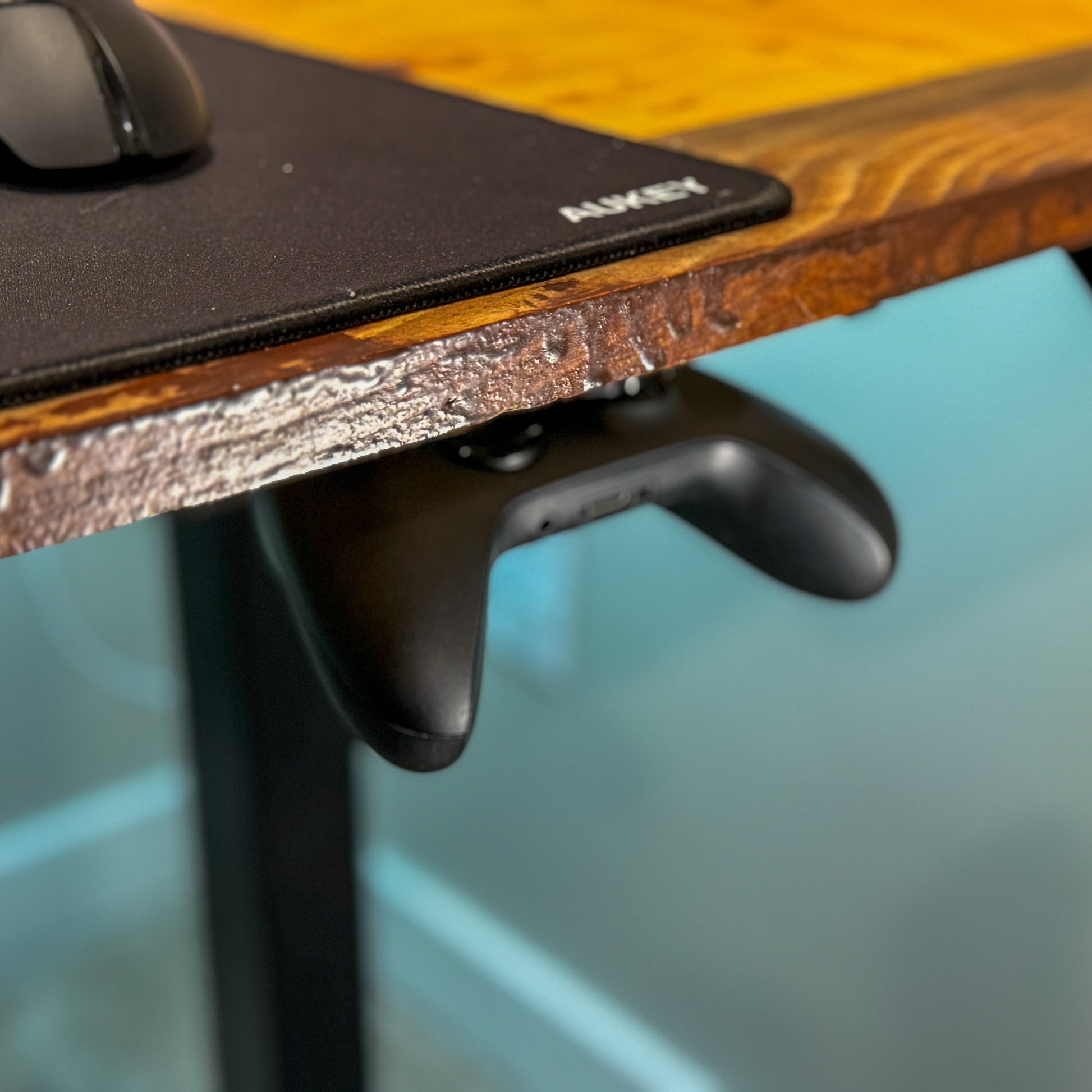 An elevated view of a black xbox controller hanging from an under desk mounted controller holder.